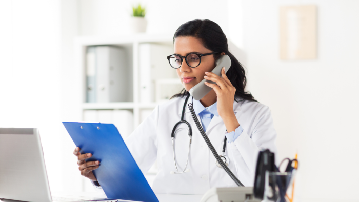Doctor on the phone with clipboard and laptop at desk