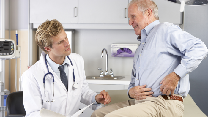 Elderly man complaining of hip pain to a male doctor.