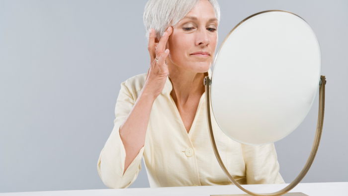 Senior woman examining her facial features in a mirror before and after Teosyal filler treatment