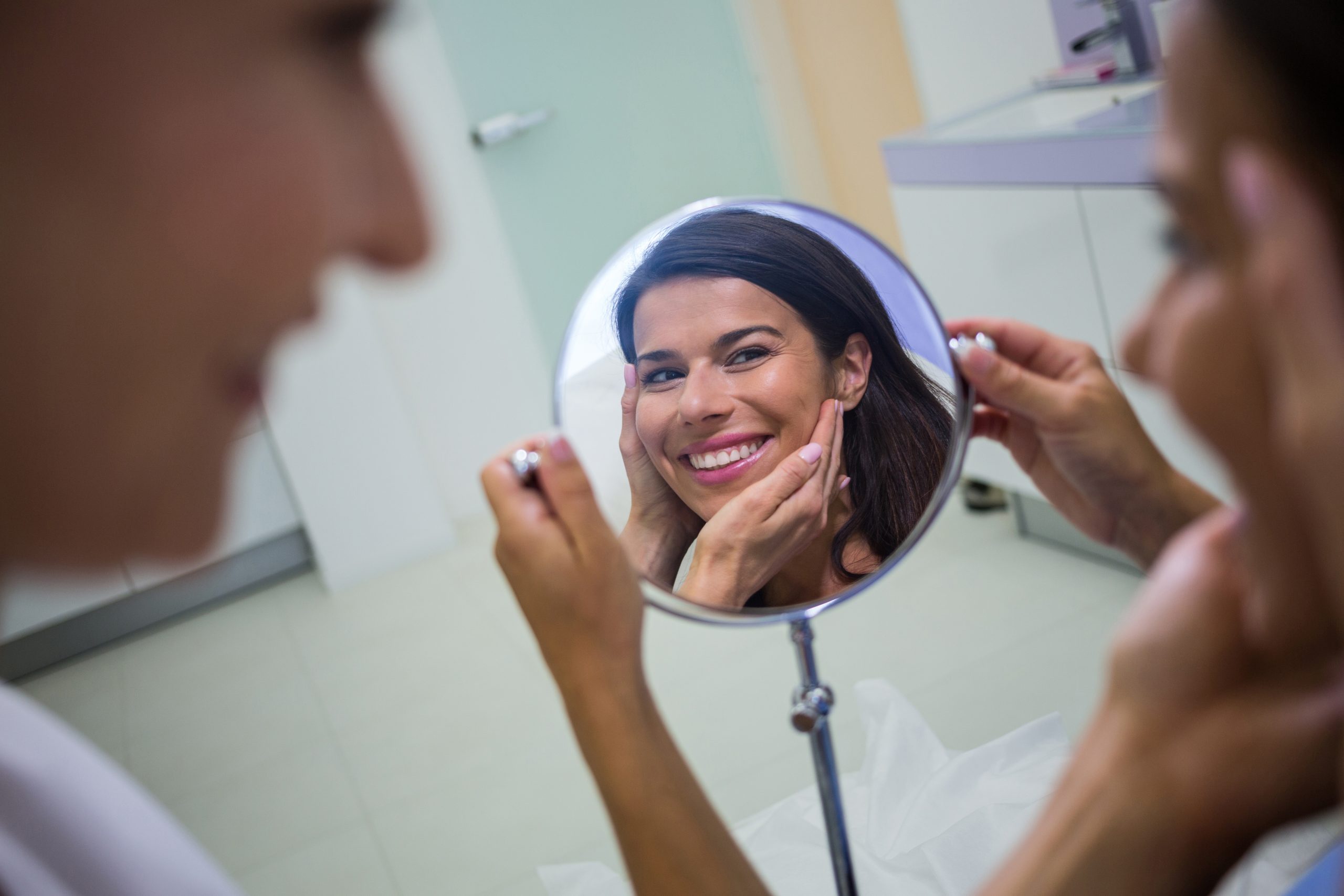 Happy woman checking her skin in the mirror after receiving cosmetic treatment