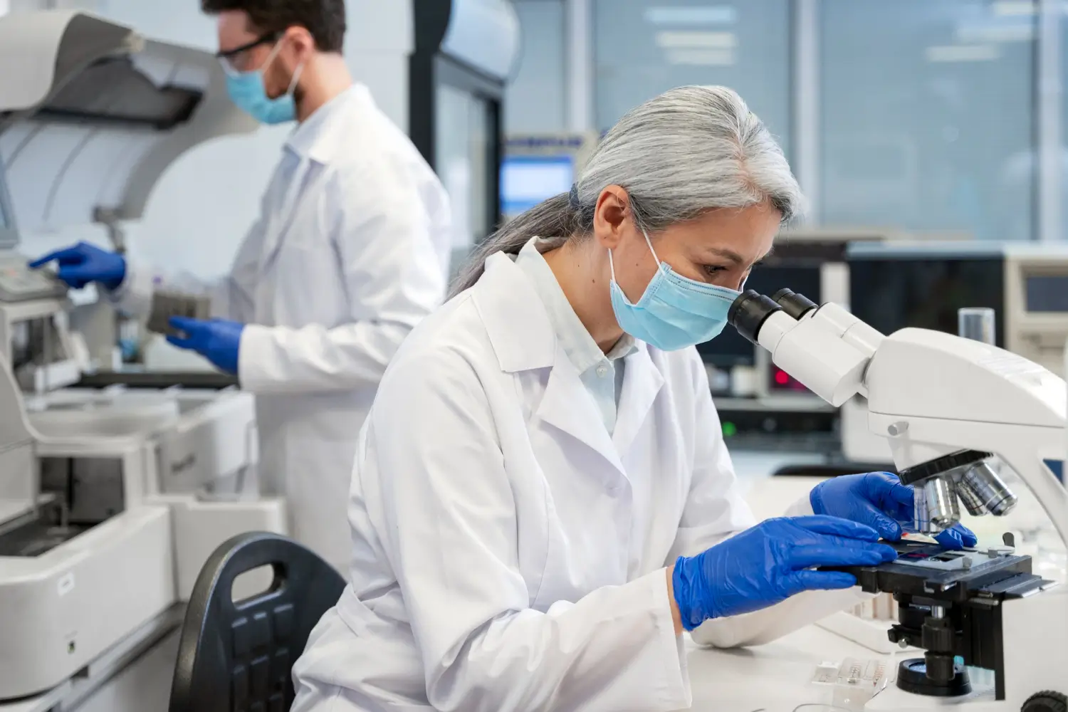 Doctors in lab coats and masks working with a microscope and lab equipment for a medical research.