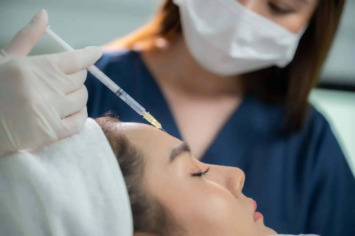 Specialist administers a treatment like Dysport to a woman's forehead.