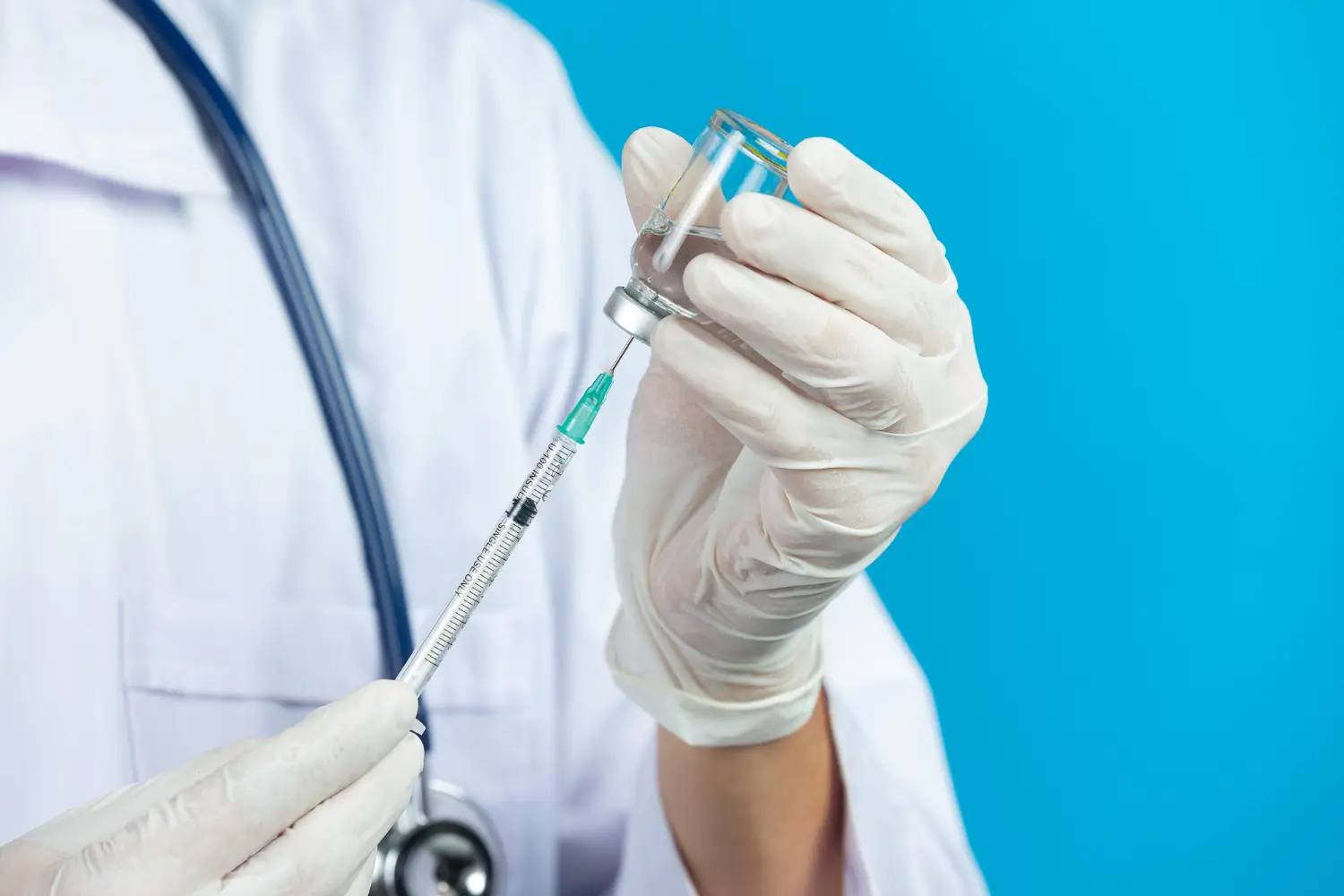 A healthcare professional wearing a white coat and gloves draws botulinum toxin like Dysport from its vial for injection